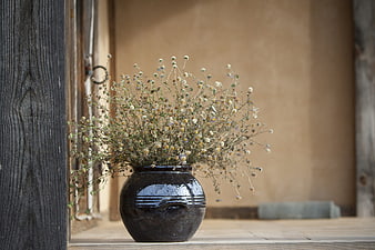 Dried wildflowers in a dark ceramic vase on a rustic wooden porch