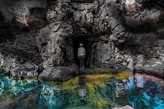 Mysterious figure standing in cave entrance with colorful water reflection