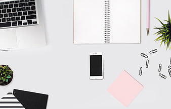 Minimalist white desk workspace with laptop, smartphone, and notebook