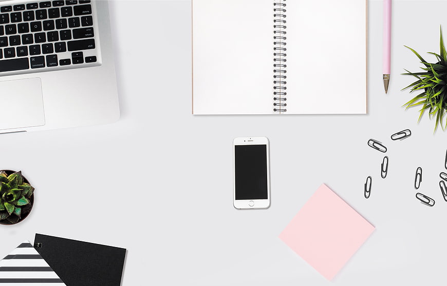 Minimalist white desk workspace with laptop, smartphone, and notebook