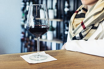 Glass of red wine on wooden table with woman in scarf