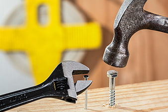 Adjustable wrench holding nail and hammer near screw on wood