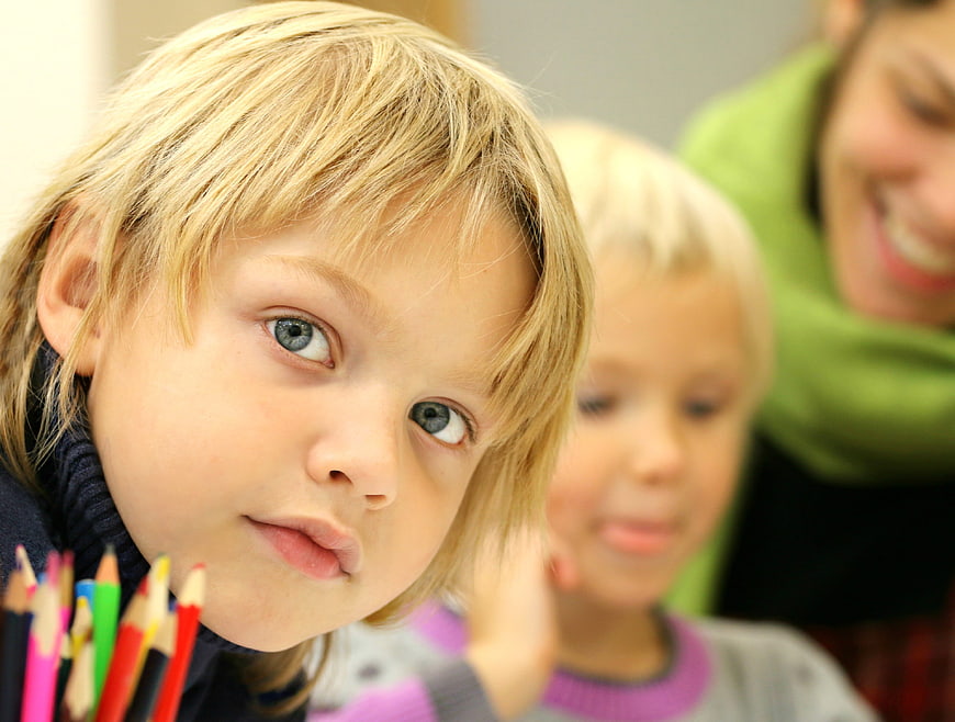 Close-up of young boy with colored pencils looking at camera
