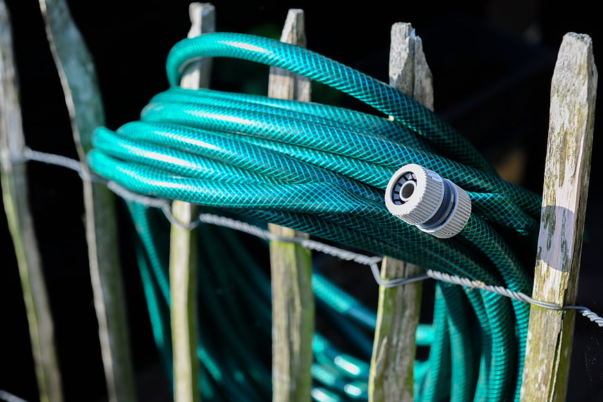 Coiled Green Garden Hose on Wooden Fence