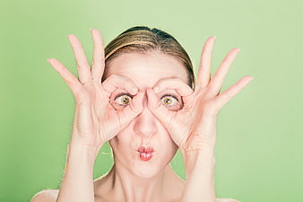 Playful Woman Making Goggles Gesture on Green Background