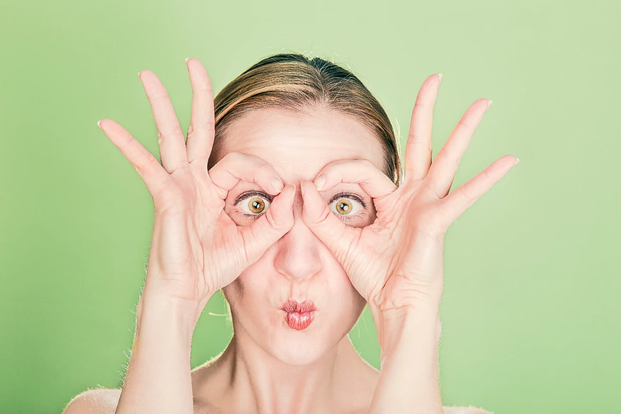 Playful Woman Making Goggles Gesture on Green Background