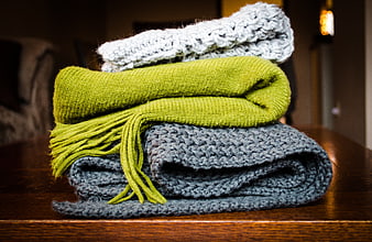 Stack of knitted scarves in green, grey, and white on wooden table