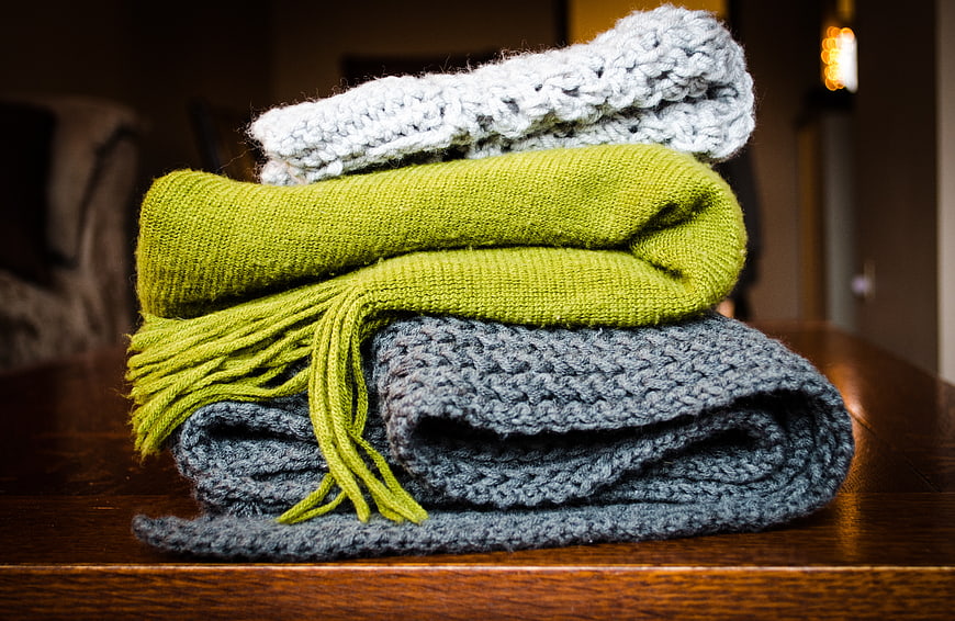 Stack of knitted scarves in green, grey, and white on wooden table