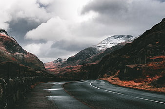 Winding Road Through Snow-Capped Mountains Under Dramatic Clouds