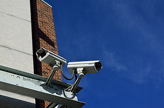 Two white security cameras mounted on a building against a blue sky