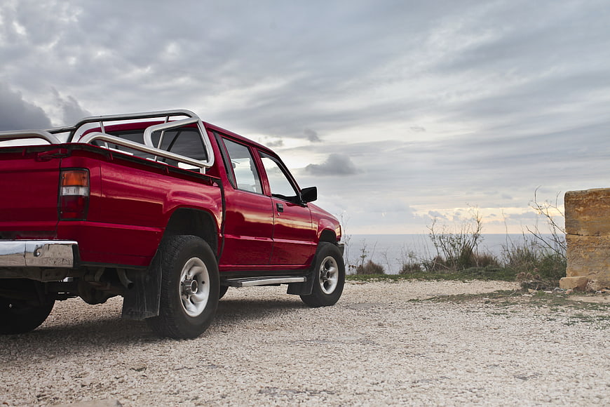 Red Pickup Truck Parked on Gravel Road Near Ocean