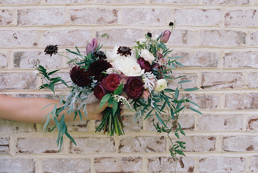 Rustic Wedding Bouquet With Dark Red And White Flowers Against Brick Wall