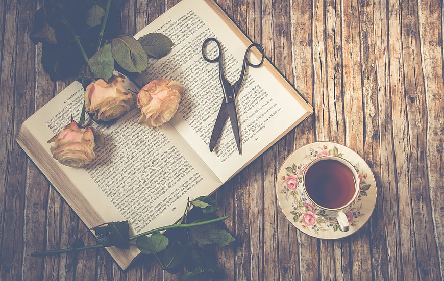 Vintage flat lay of open book, dried roses, scissors, and tea