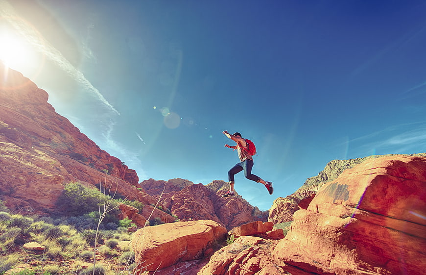Man jumping between red rocks in desert canyon