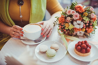 Woman holding coffee cup with macarons and bouquet on table