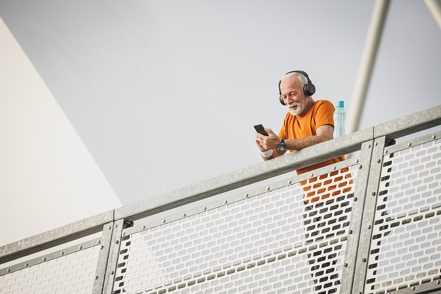 Senior man with headphones using smartphone on bridge