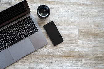 Flat lay workspace with laptop, smartphone, and camera lens on wood