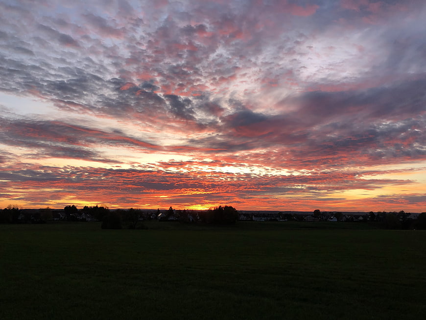 Dramatic sunset with vibrant orange and pink clouds over a dark field