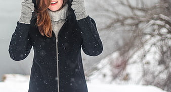 Woman in black winter coat and gray turtleneck in falling snow