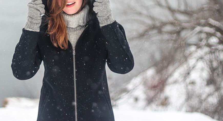 Woman in black winter coat and gray turtleneck in falling snow