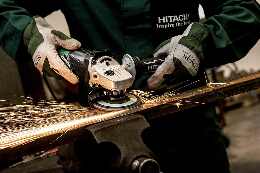 Close-up of worker using Hitachi angle grinder on metal with sparks