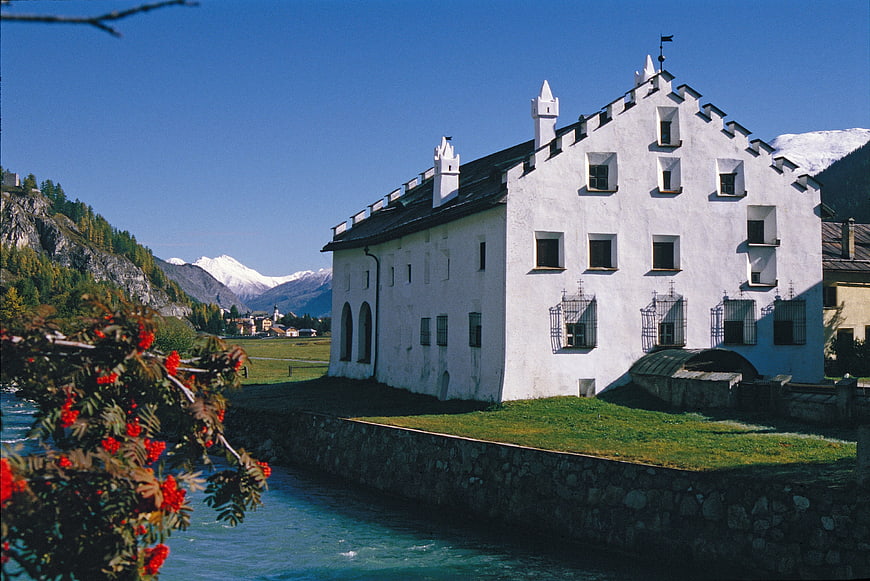 Historic white building by a river with mountains