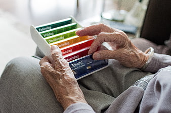 Elderly Woman's Hands Holding Color-Coded Weekly Pillbox