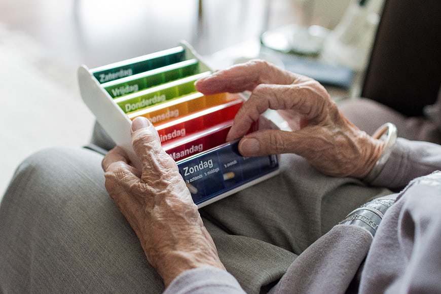 Elderly Woman's Hands Holding Color-Coded Weekly Pillbox