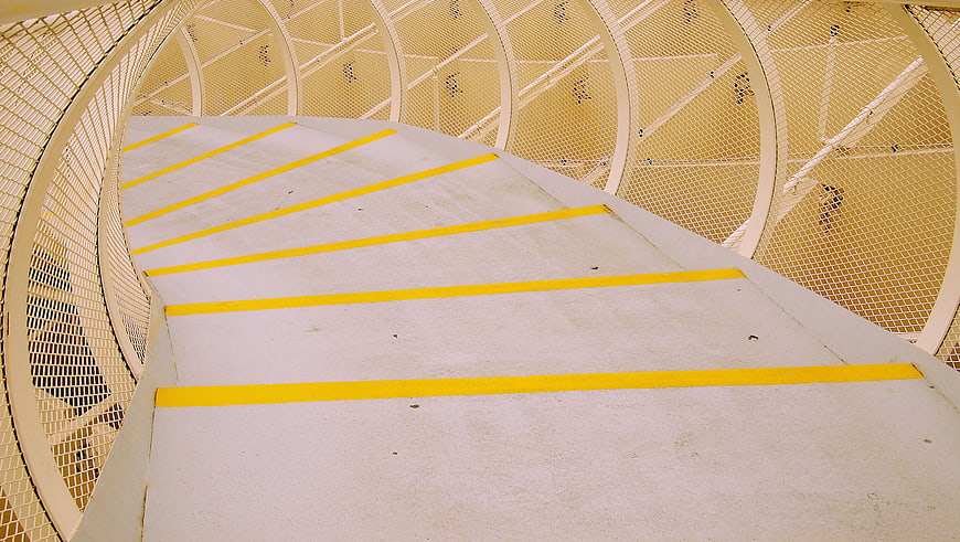 Curved concrete walkway with yellow safety stripes and metal mesh railing