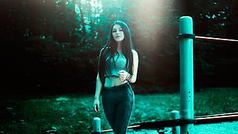 Young woman in jeans and crop top standing in a park at night