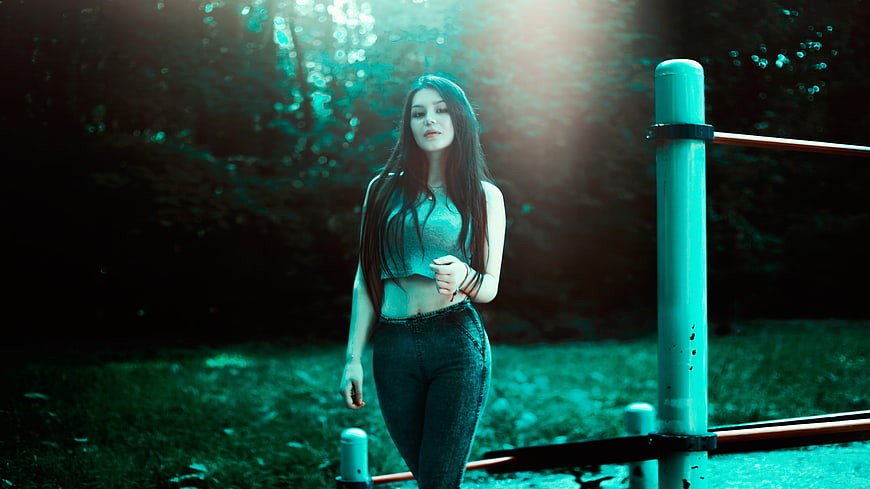 Young woman in jeans and crop top standing in a park at night