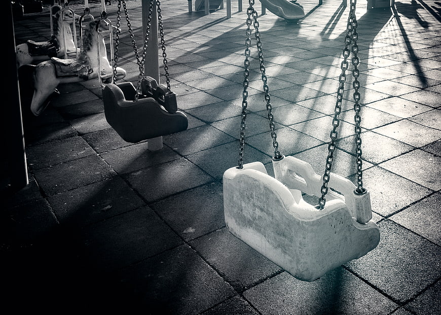 Empty playground swings in black and white with dramatic shadows