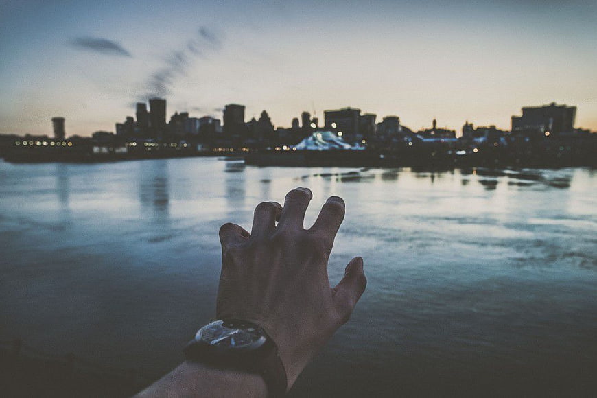 Hand with Watch Reaching Towards City Skyline at Dusk