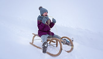 Excited young girl screaming while sledding down a snowy hill