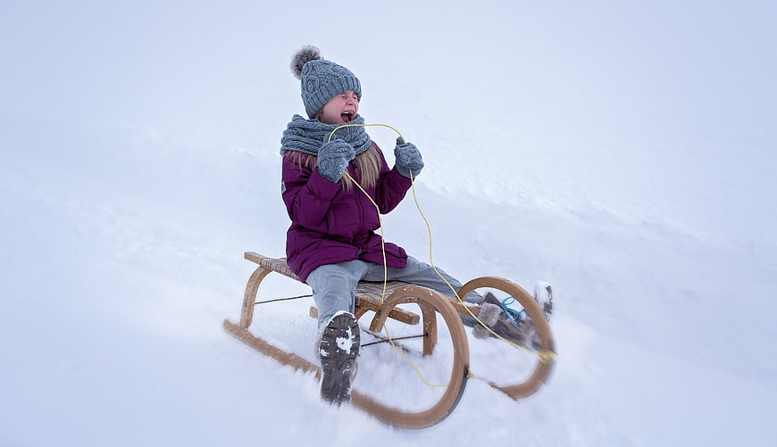 Excited young girl screaming while sledding down a snowy hill
