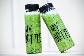 Two glass bottles filled with green smoothie and black caps
