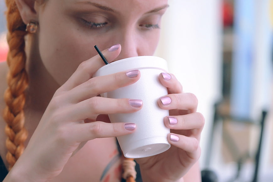 Close-up of woman with pink nails drinking from white cup