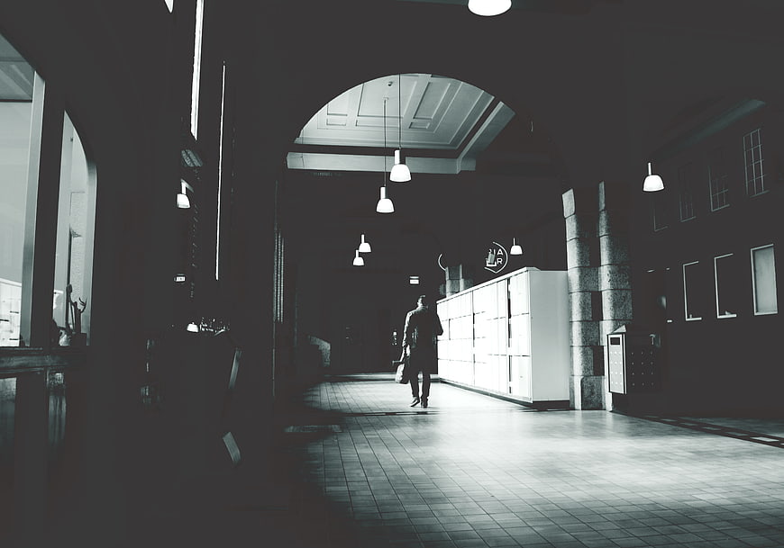 Man Walking Away in Dark Architectural Corridor