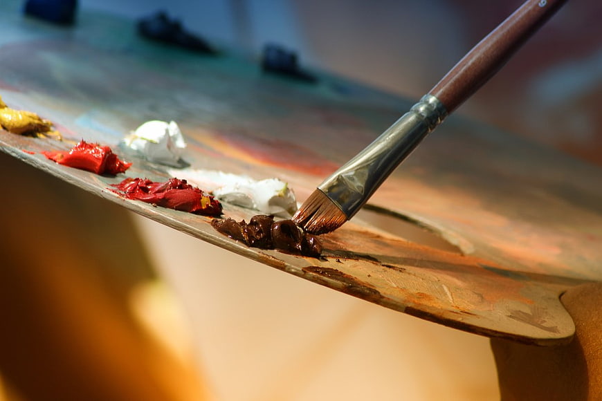 Close-up of paintbrush mixing brown oil paint on wooden palette