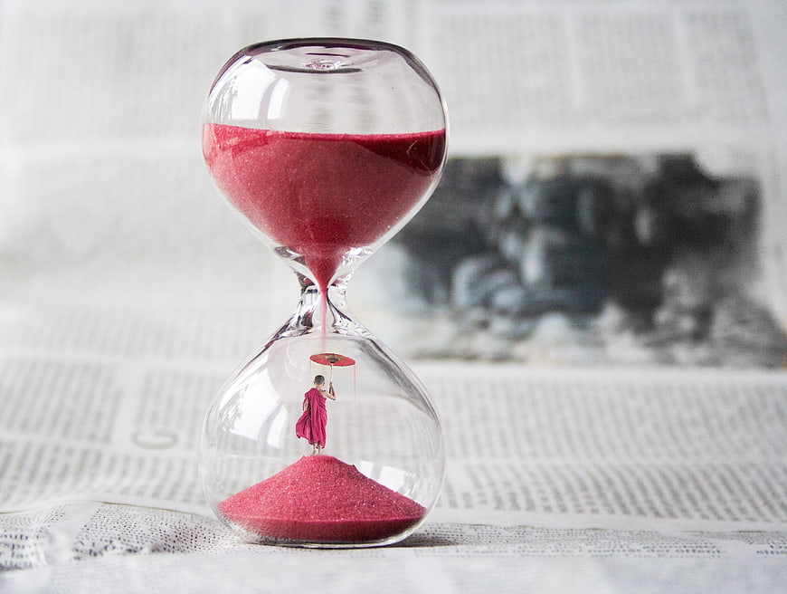 Miniature monk with umbrella inside hourglass on newspaper