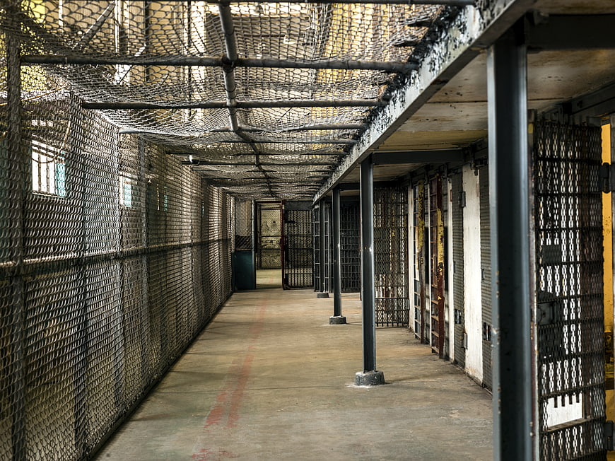 Empty prison cell block with iron bars and mesh ceiling