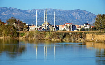 Mosque with minarets reflected in calm river water with mountain backdrop