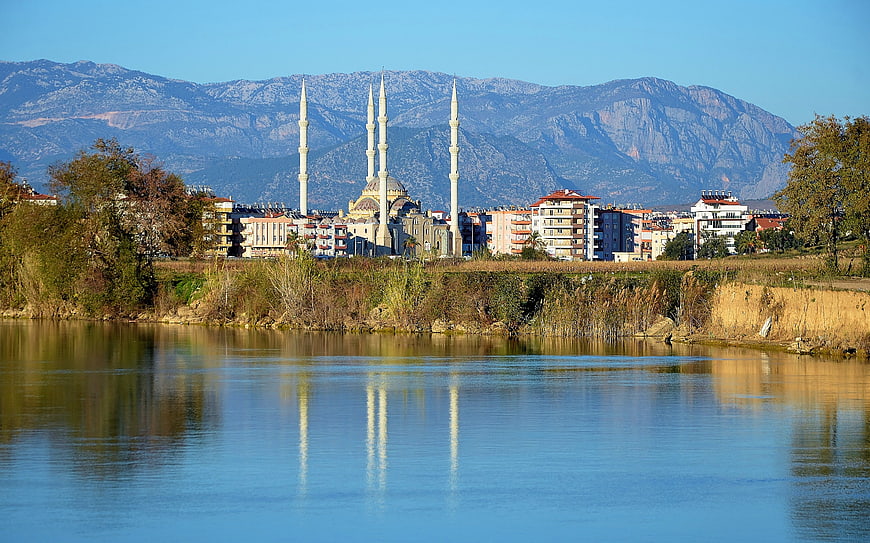 Mosque with minarets reflected in calm river water with mountain backdrop