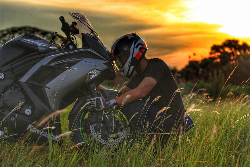 Motorcyclist Inspecting Kawasaki Ninja 650 in Tall Grass at Sunset