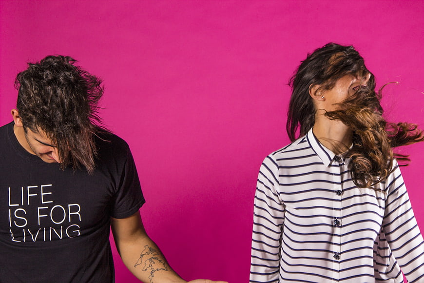 Young couple dancing with hair in motion against vibrant pink background