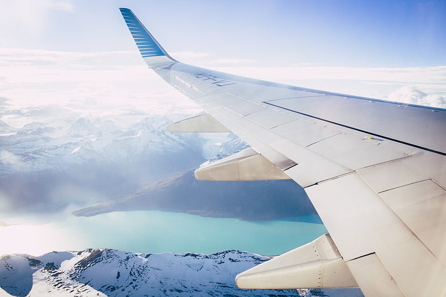Airplane wing view over snowy mountains and turquoise lake