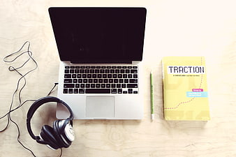 Flat lay of laptop, headphones, and business book on wooden desk