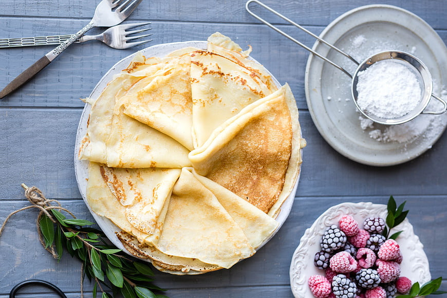 Stack of Crepes with Frozen Berries and Powdered Sugar