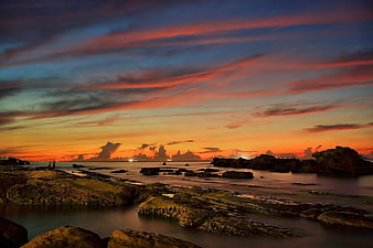 Dramatic Orange Sunset Over Rocky Coastal Shoreline