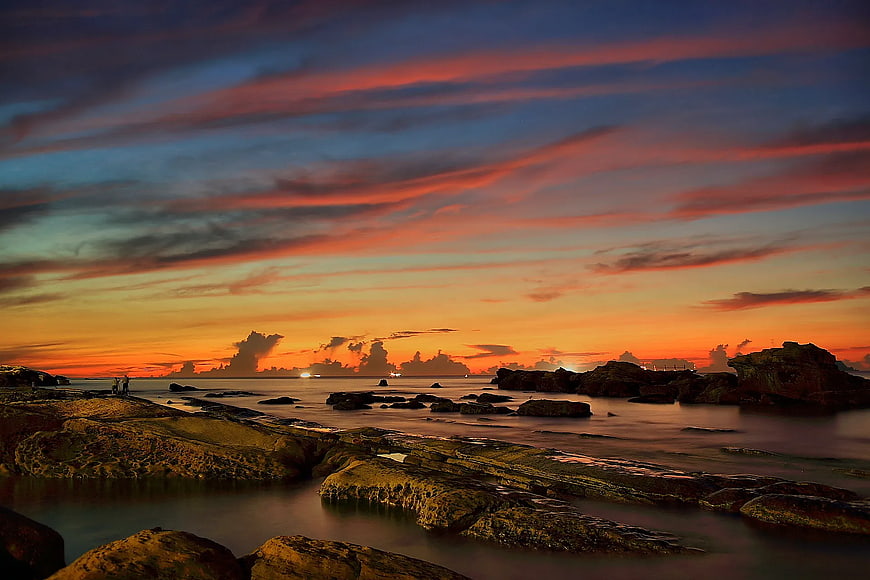 Dramatic Orange Sunset Over Rocky Coastal Shoreline